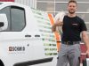Ein Mann steht vor einem Firmenwagen der Schmid AG und hält sein benötigtest Material bereit.