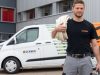 Ein Mann steht vor einem Firmenwagen der Schmid AG und hält sein benötigtest Material bereit.